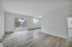 Bright interior space featuring wood-finish flooring, a sliding glass door to a balcony with a black metal railing, and white baseboard trim - 