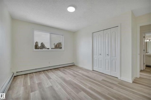 Spacious room featuring light-tone wood-finish flooring, white walls, and a large window - #10 4616 47 St, Leduc, AB - Indoor Photo Showing Other Room