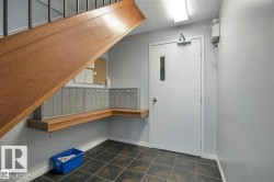 Common area entryway featuring a wood staircase, individual mailboxes on a wood shelf, and dark square floor tiles - 
