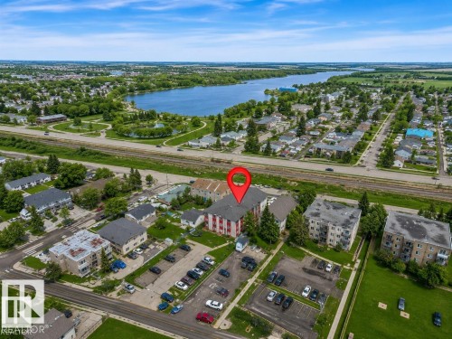 Aerial perspective showcasing a multi-story residential building with red siding and grey roofing, featuring an adjacent surface parking lot - #10 4616 47 St, Leduc, AB - Outdoor With Body Of Water With View