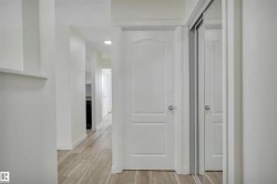 Hallway with light wood-finish flooring, white walls, and a white two-panel door with a silver knob - 
