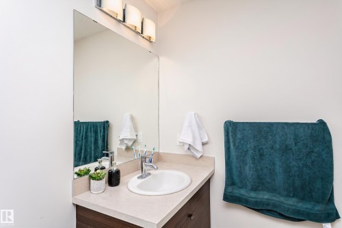 Bathroom vanity featuring a light-toned countertop, undermount sink, and wood-finish cabinetry - #104 9519 160 Av Nw, Edmonton, AB - Indoor Photo Showing Bathroom
