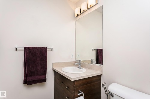 Bathroom featuring a wood-finish vanity with an integrated sink, a light-toned countertop, and a large wall-mounted mirror - #104 9519 160 Av Nw, Edmonton, AB - Indoor Photo Showing Bathroom