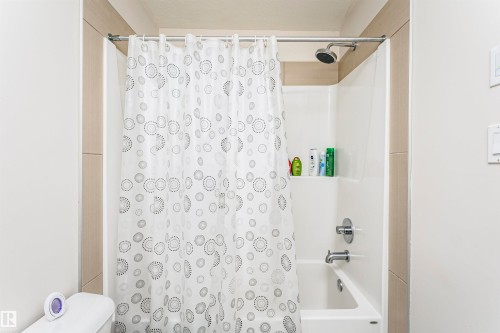 Shower/tub combination with a white acrylic surround, chrome fixtures, and a rain-style showerhead - #104 9519 160 Av Nw, Edmonton, AB - Indoor Photo Showing Bathroom