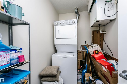 Dedicated utility space featuring a stacked washer and dryer unit, overhead ventilation system, and a metal shelving unit - #104 9519 160 Av Nw, Edmonton, AB - Indoor Photo Showing Laundry Room