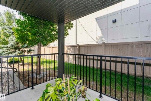 Covered patio featuring a concrete surface, black metal railing, and an overhead ceiling - #104 9519 160 Av Nw, Edmonton, AB - Outdoor