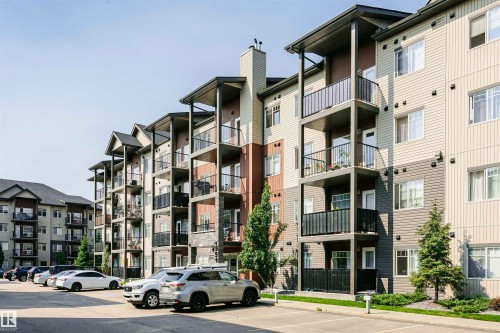 Multi-story residential building featuring horizontal siding, multiple balconies with black railings, and stone facade accents - #104 9519 160 Av Nw, Edmonton, AB - Outdoor With Facade