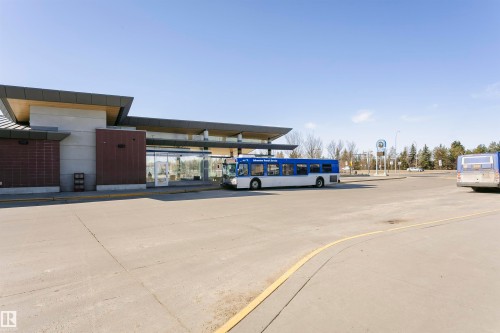 Modern transit facility featuring a large concrete parking area, extensive glass curtain walls, a flat roofline, and integrated brick accents - #104 9519 160 Av Nw, Edmonton, AB - Outdoor