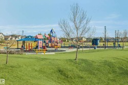 Neighborhood park featuring extensive playground equipment, multiple swing sets, covered picnic tables, and abundant open green space - 