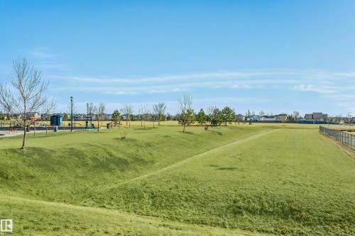 Expansive green space featuring rolling hills, varied topography, and a distant playground area with blue structures - #104 9519 160 Av Nw, Edmonton, AB - Outdoor With View