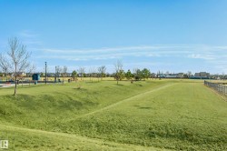 Expansive green space featuring rolling hills, varied topography, and a distant playground area with blue structures - 