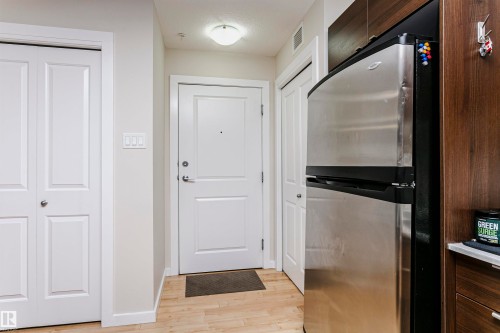 Entrance area featuring light wood-finish flooring, a contemporary flush mount ceiling light, and white paneled doors - #104 9519 160 Av Nw, Edmonton, AB - Indoor Photo Showing Other Room