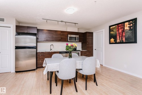 Kitchen and dining area featuring light wood-finish flooring, dark wood cabinetry, stainless steel appliances, and track lighting - #104 9519 160 Av Nw, Edmonton, AB - Indoor Photo Showing Dining Room