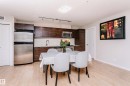 Kitchen and dining area featuring light wood-finish flooring, dark wood cabinetry, stainless steel appliances, and track lighting - #104 9519 160 Av Nw, Edmonton, AB 