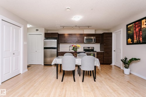 Open-concept kitchen and dining area featuring light wood-finish flooring, dark wood cabinetry, stainless steel appliances, and white countertops - #104 9519 160 Av Nw, Edmonton, AB - Indoor