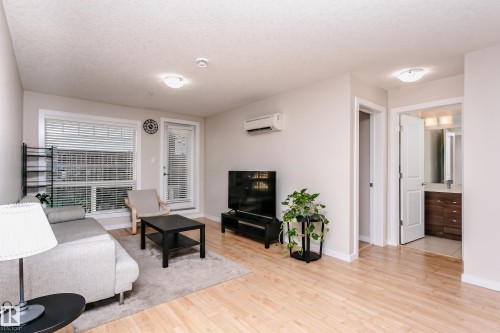 Bright living area featuring wood-finish flooring, a wall-mounted air conditioning unit, and a glass-paned exterior door - #104 9519 160 Av Nw, Edmonton, AB - Indoor Photo Showing Living Room