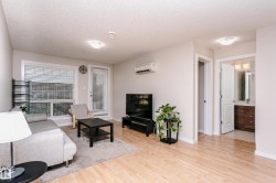 Bright living area featuring wood-finish flooring, a wall-mounted air conditioning unit, and a glass-paned exterior door - 
