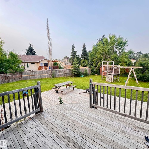 Expansive backyard oasis featuring a composite deck with black railings, manicured lawn, picnic table, and mature landscaping including evergreen and deciduous trees - 4821 11A Avenue Nw, Edmonton, AB - Outdoor With Backyard