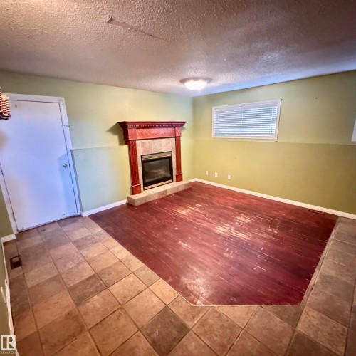 Spacious recreation room featuring a wood-finish flooring layout with contrasting tile borders, a built-in fireplace with decorative surround, and abundant natural light from multiple windows - 4821 11A Avenue Nw, Edmonton, AB - Indoor With Fireplace