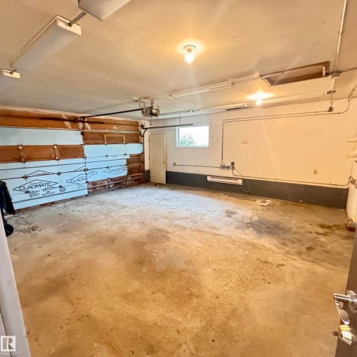 Spacious garage featuring concrete flooring, overhead door with wood-finish paneling, built-in lighting fixtures, and ample square footage for vehicle storage and workspace - 4821 11A Avenue Nw, Edmonton, AB - Indoor Photo Showing Garage