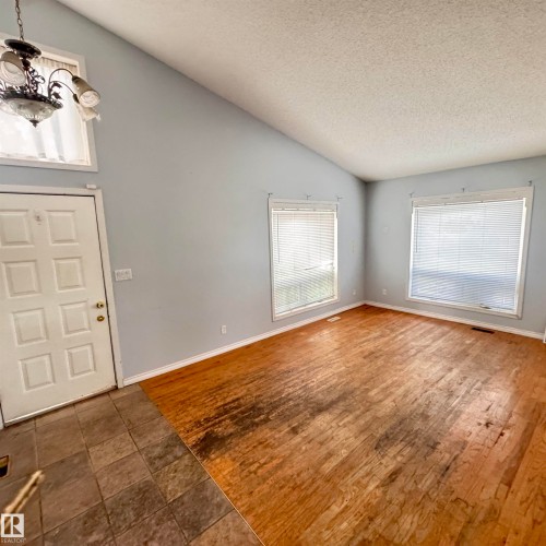 Spacious living area showcasing warm wood-finish flooring, abundant natural light from dual windows with blinds, fresh neutral wall paint, and a vaulted ceiling with recessed lighting - 4821 11A Avenue Nw, Edmonton, AB - Indoor Photo Showing Other Room
