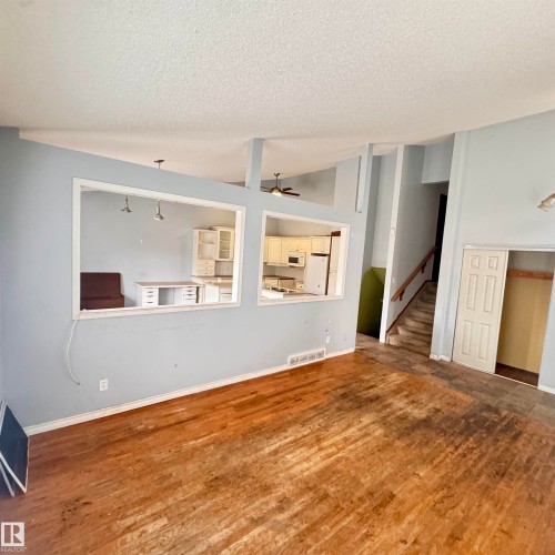 Open-concept living area featuring warm wood-finish flooring, white trim detailing, and pass-through openings to the kitchen - 4821 11A Avenue Nw, Edmonton, AB - Indoor