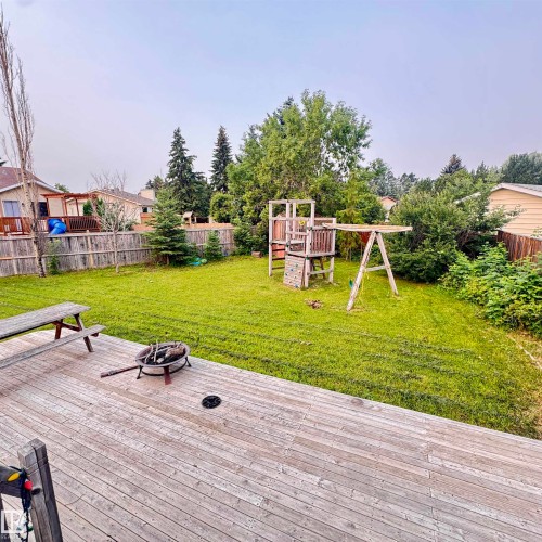Expansive backyard oasis featuring a meticulously manicured lawn, mature tree canopy, wooden play structure with swings and climbing apparatus, composite deck with integrated fire pit, and wooden bench seating - 4821 11A Avenue Nw, Edmonton, AB - Outdoor