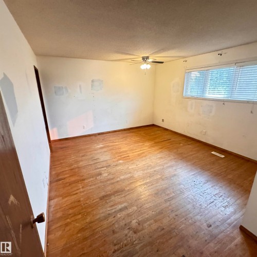 Spacious room featuring warm wood-finish flooring, abundant natural light from large windows with blinds, ceiling fan with flush-mount fixture, and fresh neutral walls - 4821 11A Avenue Nw, Edmonton, AB - Indoor Photo Showing Other Room