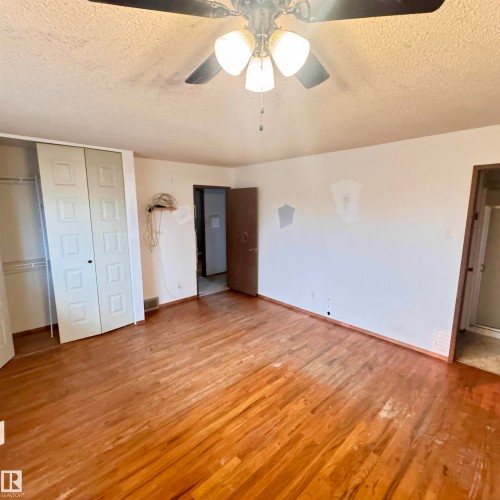 Spacious bedroom featuring hardwood flooring, ceiling fan with integrated lighting, and multiple closet options including double-door and single-door configurations - 4821 11A Avenue Nw, Edmonton, AB - Indoor Photo Showing Other Room