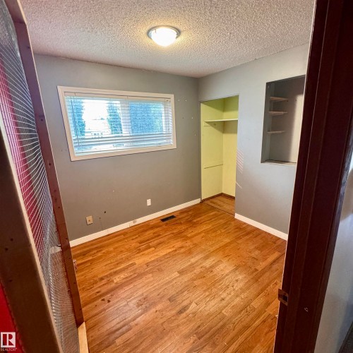 Room featuring wood-finish flooring, a window with horizontal blinds, built-in open shelving, and an integrated closet with shelving - 4821 11A Avenue Nw, Edmonton, AB - Indoor Photo Showing Other Room