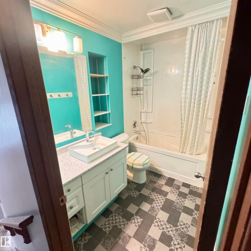 Bathroom featuring patterned floor tiling, a white vanity with cabinet storage and a vessel sink, a shower-tub combination, and built-in wall shelving - 4821 11A Avenue Nw, Edmonton, AB - Indoor Photo Showing Bathroom