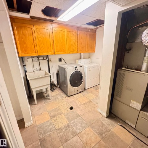 Dedicated laundry room featuring wood-finish cabinetry, tile flooring, and built-in appliances including a front-load washer, electric dryer, and utility sink - 4821 11A Avenue Nw, Edmonton, AB - Indoor Photo Showing Laundry Room