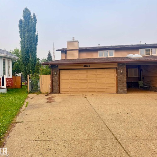 Welcoming front elevation showcasing a two-car garage with wood-finish doors, brick and horizontal siding exterior, and mature landscaping including a tall columnar evergreen - 4821 11A Avenue Nw, Edmonton, AB - Outdoor