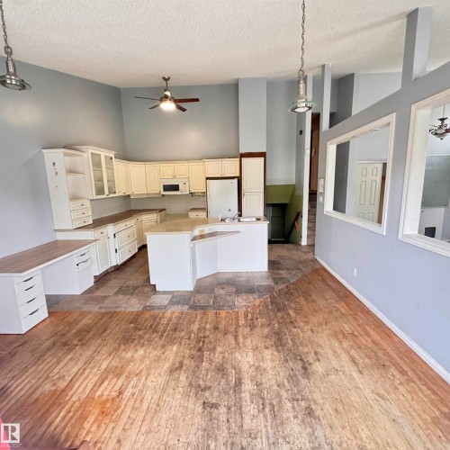 Kitchen featuring white cabinetry with some glass-front doors, light-toned countertops, and a central island with a breakfast bar extension - 4821 11A Avenue Nw, Edmonton, AB - Indoor Photo Showing Kitchen