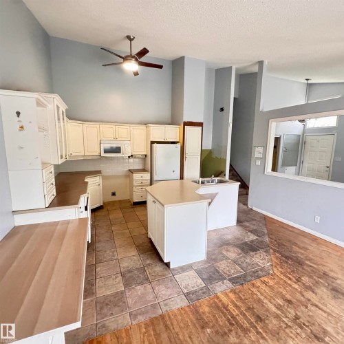 Open-concept kitchen with vaulted ceilings, featuring white cabinetry, a built-in microwave, and an island with an integrated sink - 4821 11A Avenue Nw, Edmonton, AB - Indoor Photo Showing Kitchen