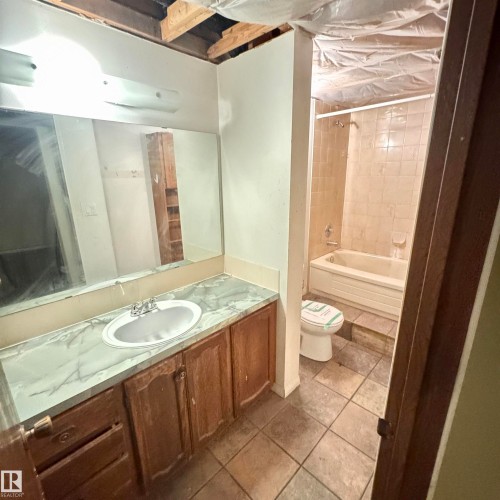 Spacious primary bathroom featuring a wood-finish vanity with dual-sink marble countertop, large framed mirror, and ceramic tile flooring - 4821 11A Avenue Nw, Edmonton, AB - Indoor Photo Showing Bathroom