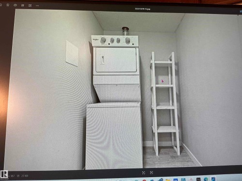 Dedicated laundry area featuring a stacked washer and dryer unit, light-toned wall paint, and wood-finish flooring - #106 592 Hooke Rd Nw, Edmonton, AB 