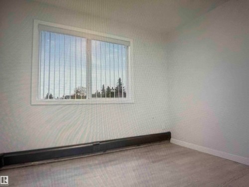 Room featuring wood-finish flooring, a baseboard heating unit, and a window with vertical blinds - #106 592 Hooke Rd Nw, Edmonton, AB 