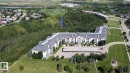 Expansive multi-story building featuring a pitched roof, multiple balconies, and a paved parking area with covered spaces - #106 592 Hooke Rd Nw, Edmonton, AB  - Outdoor With View 
