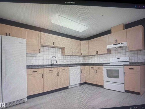Kitchen featuring extensive light wood-finish cabinetry, dark countertops, white square tile backsplash, and a modern black faucet - #106 592 Hooke Rd Nw, Edmonton, AB 