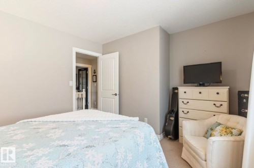 Neutral-toned bedroom featuring carpeted flooring and an open doorway leading to a hallway with a staircase - 22 Voleta Crest, Spruce Grove, AB - Indoor Photo Showing Bedroom