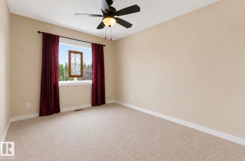 Neutral-toned room featuring a large window with a decorative stained-glass accent, a ceiling fan with integrated lighting, and carpeted flooring - 22 Voleta Crest, Spruce Grove, AB - Indoor Photo Showing Other Room