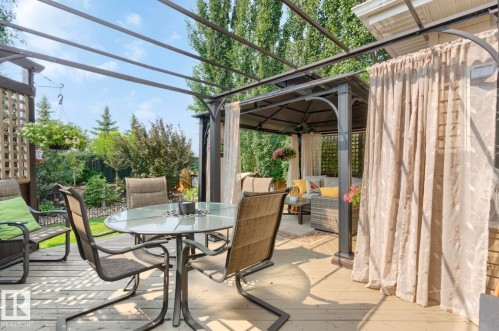 Expansive outdoor entertaining space featuring a pergola-covered patio with integrated curtain system, metal-frame dining table with seating for six, and mature landscaping - 22 Voleta Crest, Spruce Grove, AB - Outdoor With Deck Patio Veranda With Exterior