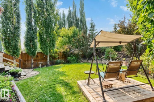 Expansive backyard oasis featuring a manicured lawn, mature poplar and evergreen trees providing natural privacy screening, paved patio area with pergola and shade canopy, and established landscaping with ivy-covered fencing and garden beds - 22 Voleta Crest, Spruce Grove, AB - Outdoor With Backyard