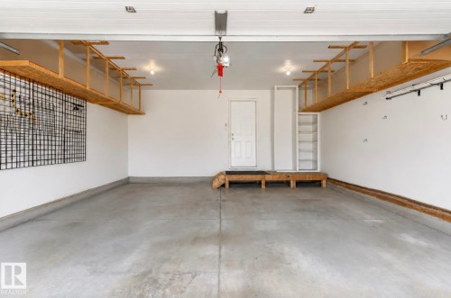 Spacious garage featuring polished concrete flooring, overhead storage shelving with wood-finish framing, recessed ceiling lighting, and direct interior access - 22 Voleta Crest, Spruce Grove, AB - Indoor Photo Showing Garage