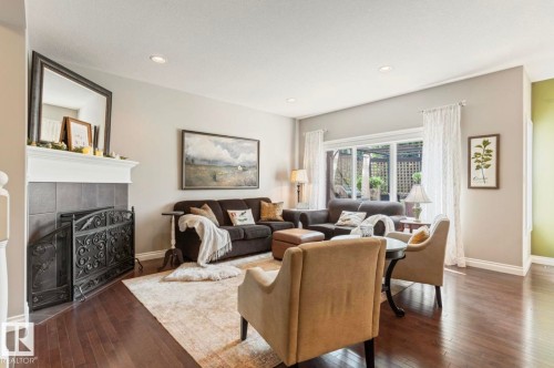 Elegant living room showcasing hardwood flooring, a decorative fireplace with tile surround, and large multi-pane windows with white trim and drapery - 22 Voleta Crest, Spruce Grove, AB - Indoor Photo Showing Living Room With Fireplace