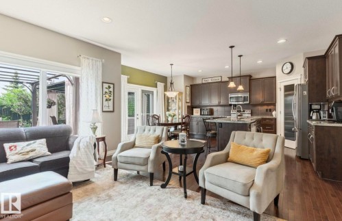 Open-concept living space featuring dark wood-finish flooring, a kitchen with dark cabinetry and stainless steel appliances, a kitchen island with seating, recessed lighting, and a glass-paneled door leading to an outdoor area - 22 Voleta Crest, Spruce Grove, AB - Indoor
