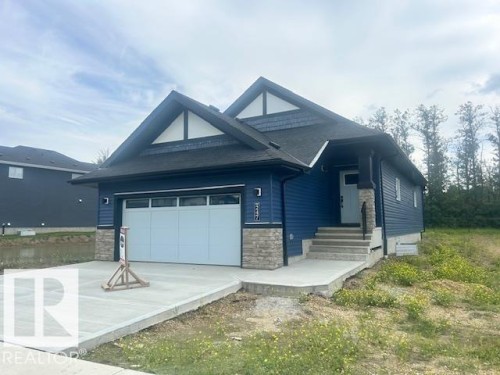 Contemporary-style residence featuring a bold blue siding, decorative gable accents, an attached garage, a concrete driveway, and a stone-clad entry column - 247 Edgemont Green Green Nw, Edmonton, AB 