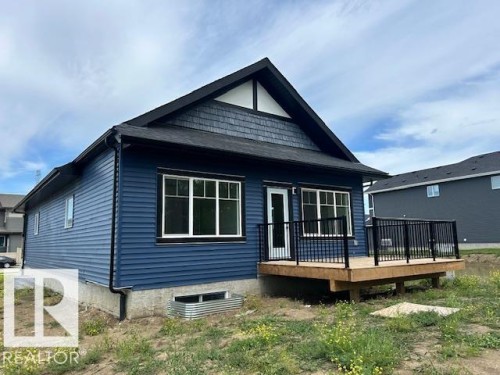 Rear exterior featuring a wood deck with black metal railings, dark blue horizontal siding, and a gabled roofline with dark shingles and shake siding accents - 247 Edgemont Green Green Nw, Edmonton, AB 