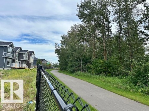 Paved pathway bordering green space and mature trees, featuring chain-link fencing - 247 Edgemont Green Green Nw, Edmonton, AB 